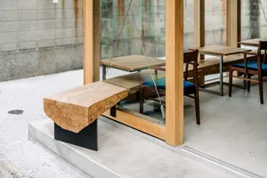 A modern restaurant interior featuring wooden tables and chairs with metal details, view from the exterior.