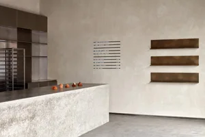 Modern, minimalist café interior featuring concrete countertops and brass accents with a menu board and pastries on display.