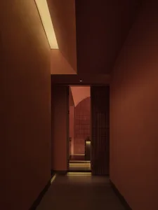 Interior view of a minimalist corridor with red tiles and concrete floor, showcasing linear lighting and geometric design.