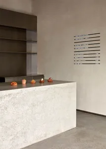 A clean, minimalist coffee shop with a concrete counter featuring pastries and a menu board on the wall.