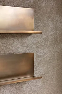 A modern, metal shelf mounted on a textured wall.
