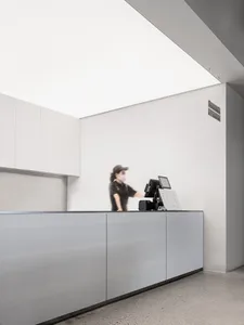 A minimalist modern reception counter with a concrete and white surface, featuring a digital display and a person wearing a f