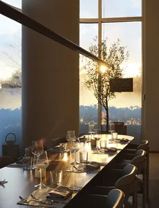 A modern restaurant dining room with a long wooden table, chairs, and place settings, featuring a large window with a view of
