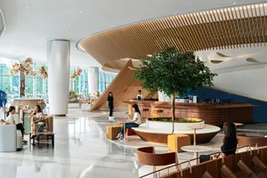 A modern cafe interior with wooden elements, glass tables, metal seating, and green plants.