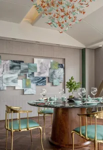 A modern dining room with a round table made of marble and gold chairs with teal cushions.