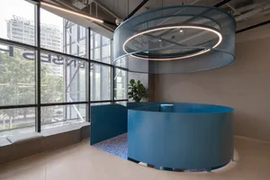 A modern office space with a blue circular reception desk, large windows, and a hanging circular light fixture.