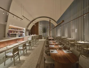 Modern restaurant interior with wooden tables, glass walls, and fabric seating.