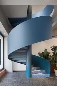 A modern, blue metal spiral staircase with a sleek design and a smooth, curved wall.