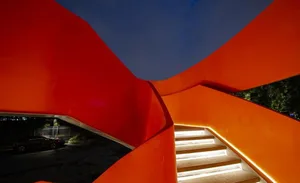 An image of a modern, metallic staircase with orange railings.