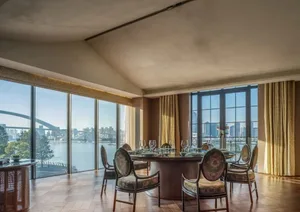 Modern dining room with elegant chairs, round table, and glass windows overlooking a scenic cityscape.