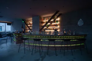 Industrial bar interior with brick walls, concrete counter, and glass shelves.