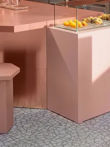 A minimalist retail space featuring metallic pink materials and a glass display case with food items.