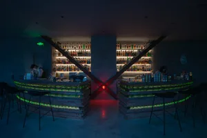 Modern bar interior with brick counter and concrete walls, illuminated by green and red lights.