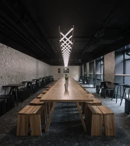 Long wooden dining table with benches and stools in a modern restaurant setting.