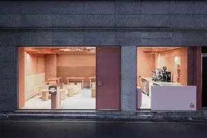 A minimalist coffee shop interior with a pink metallic door and pink steel accents.