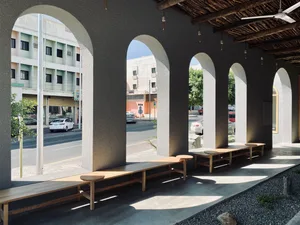 A row of arches made from concrete with wooden benches and a wooden ceiling in an urban public space.