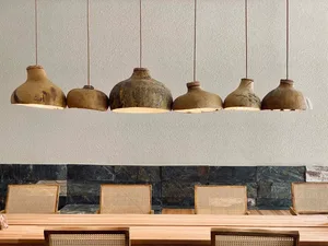 A row of rustic, handmade clay pendant lights hang above a dining table in an industrial-themed restaurant interior.