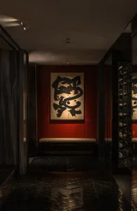 A corridor with a metallic tiled floor, red walls, and a large abstract painting on the wall.