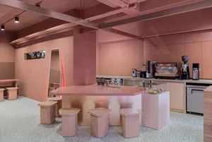 A minimalist coffee shop with pink walls, hexagonal stools, and industrial design elements.