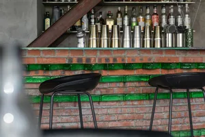 A modern bar counter made of brick, with green accents and various containers and bottles on the shelf.