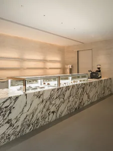 A modern marble coffee shop counter with glass display cases displaying pastries and desserts.