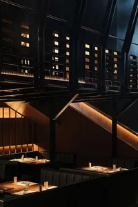 Interior of a modern restaurant featuring black furniture, wooden panels, and a warm, ambient lighting setup.