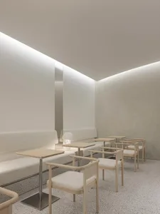 White-themed restaurant interior with minimalist design, wooden chairs, and fabric seating.