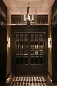 Modern entrance lobby featuring glass doors with a sleek steel frame, illuminated by contemporary lighting fixtures and a pat