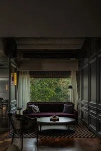 A modern living room featuring a purple sofa, coffee table, and wood flooring, with a view of greenery outside.