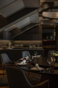 Modern dining room with wooden furniture, glassware, and a sleek kitchen in the background.