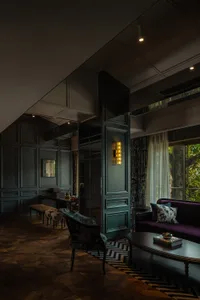 A modern living room with dark interior design features a comfortable purple couch, a stylish wooden chair, and a well-lit sp