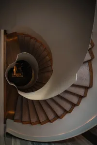 A spiral staircase with carpeted steps viewed from above, highlighting the intricate design and the contrast between the wood
