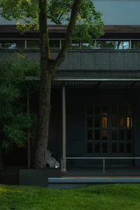 A modern building exterior with a concrete porch and a tree in a small garden.