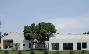 A modern home with a white exterior, concrete walls, and large glass windows against a blue sky.
