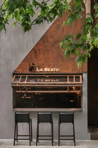 Outdoor seating area with black leather stools in front of a metal-framed storefront with a cat logo and the word 'La Beato'.