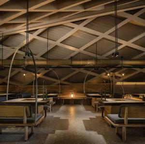 Industrial-style restaurant interior with wooden tables, arched ceiling, and hanging lights.