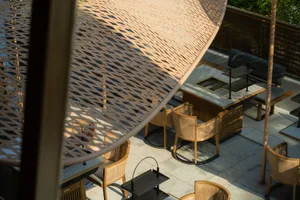 Luxury outdoor dining area featuring modern, wooden furniture and a woven table umbrella.