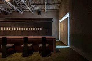 Modern minimalist restaurant interior with dark wood seating and concrete walls.