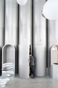 A minimalist coffee shop interior with tall metal cylindrical columns and round hanging lights