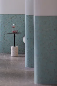 A modern coffee shop featuring a sleek, black table with a vase and two cups on a concrete cylinder base, against a speckled 