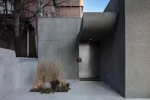 A modern concrete entranceway with a sleek, stainless-steel door and minimalist landscaping.