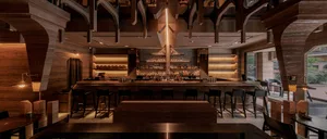A modern restaurant bar with a wooden counter, metallic accents, and glass shelving.