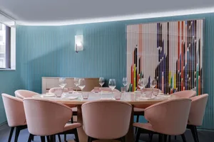 A modern restaurant dining room with a round wooden table surrounded by pink fabric chairs, decorated with wine glasses and p