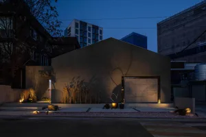 Modern storefront with concrete walls at dusk with illuminated plants and lights.