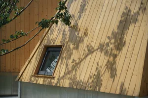 A wooden house extension with a unique triangular roof section, featuring a small window.