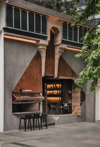 A modern cafe exterior with a concrete facade and arched windows, featuring a bar counter with stools.