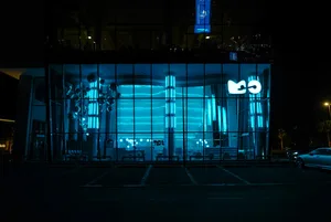 Modern, minimalist building exterior illuminated with blue glass lights at night.