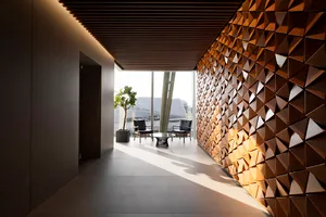 A modern office space featuring a wall made of wooden triangles and a small sitting area with chairs and a plant.