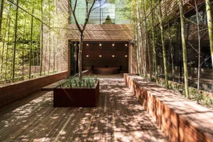 Modern apartment with brick walls and a wooden deck surrounded by bamboo plants.