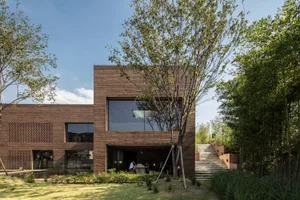 A modern, brick building with large windows surrounded by greenery and steps.